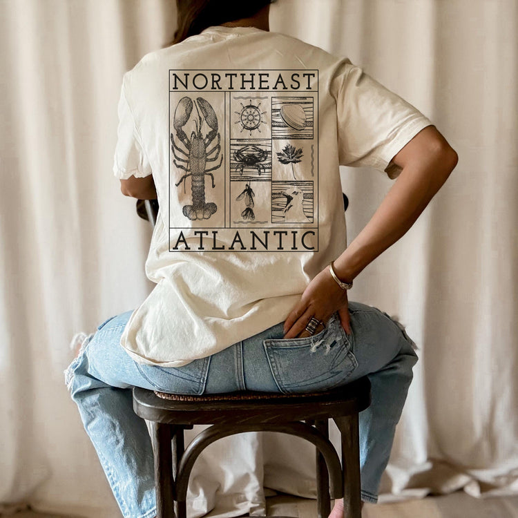 Back view of the Northeast Atlantic design on an ivory-color tee. This shirt celebrates the coasts of our northeastern states by highlighting an iconic lobster, ship wheel, a squawking seagull, a crab, maple leaf, clam, and polynoses