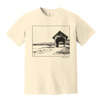 Front view of the Covered Bridge cotton t‑shirt in Ivory (cream), with a storybook scene of a rustic covered bridge arching over a quiet Vermont dirt road.