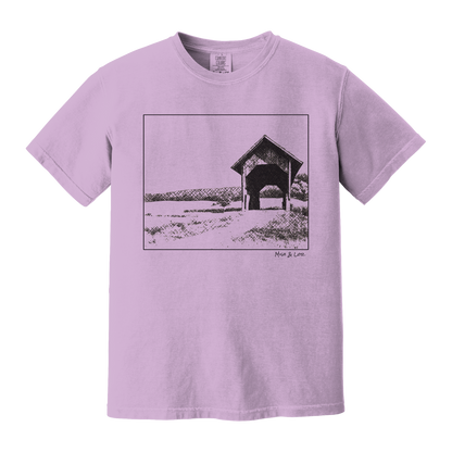 Front view of the Covered Bridge cotton t‑shirt in Orchid (purple), with a storybook scene of a rustic covered bridge arching over a quiet Vermont dirt road.