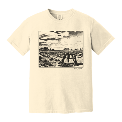 Desert Horse t-shirt in Ivory (cream), with a lone horse grazing before desert buttes under a softly clouded southwestern sky.