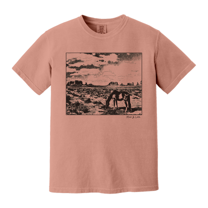 Desert Horse t-shirt in Terracotta (coral), with a lone horse grazing before desert buttes under a softly clouded southwestern sky.