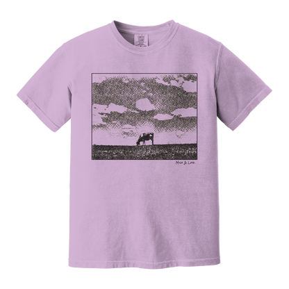 Front view of the Field Cow Cotton T-Shirt in Orchid (purple) featuring  a whimsical black-and-white rendering of a lone cow grazing in a field beneath a cloud-dotted sky