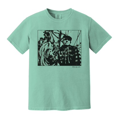 Front view of the Fisherman Cotton T-Shirt in Chalky Mint (green), featuring a vintage portrait of a fisherman in flannel, gripping ropes on a boat with a cigar in his mouth.