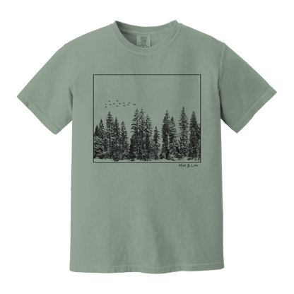 Front view of the Flight Over Evergreens Cotton T-shirt in Bay (green), featuring a framed graphic of birds flying low over a line of PNW forest.