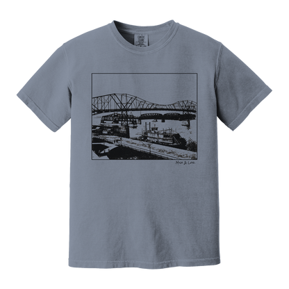 Front view of the Mississippi River Bride Cotton T-Shirt in Blue Jean (dusty blue), featuring a framed vintage riverfront scene — steel bridges and riverboats rendered in a minimalist, indie-inspired style