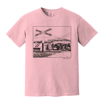 Front view of the Railroad Crossing cotton t-shirt in Blossom (pink), featuring a railroad crossing sign in front of a hillside covered bridge — a quiet Vermont scene
